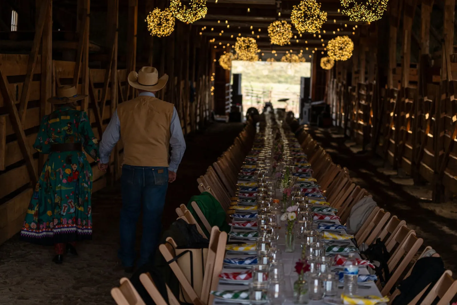 The long communal dinner table set under string lights inside the barn