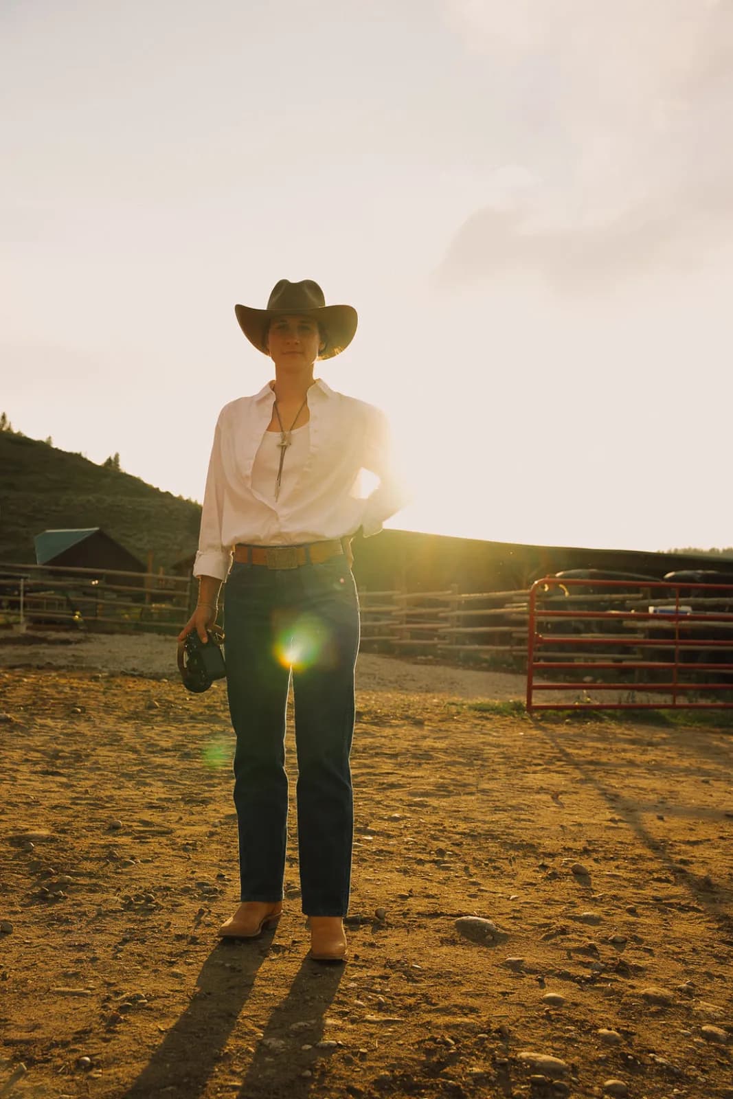 A guest in a cowboy hat backlit by the setting sun in the corral