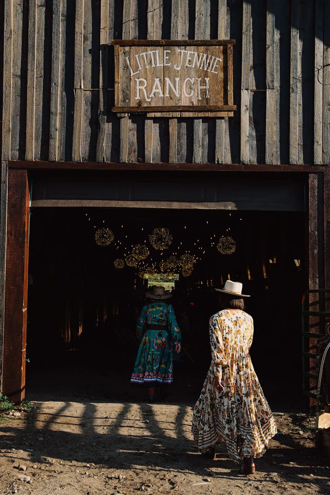 Two guests in vintage dresses stepping into the lantern-lit barn