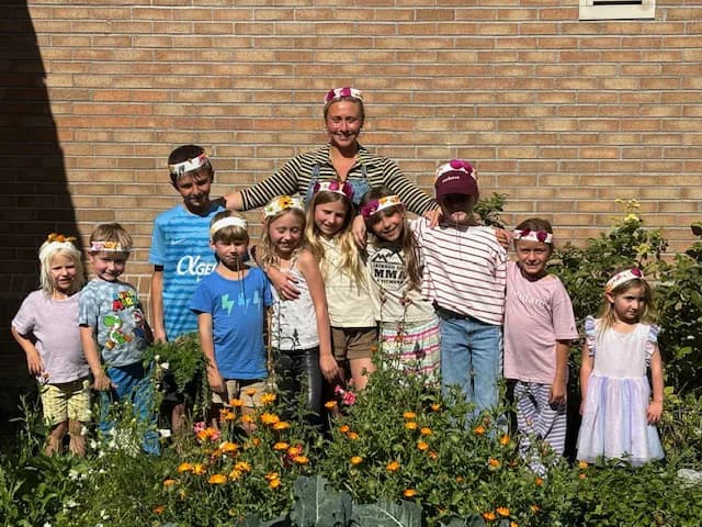 Kids and their teacher posing among blooming flowers in the community garden
