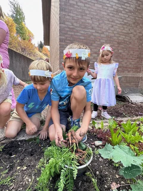Children proudly holding freshly harvested carrots from the garden