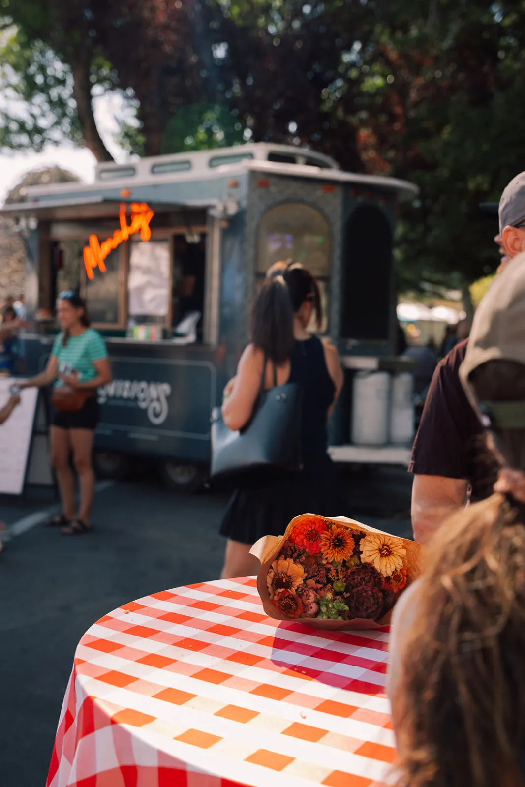 A food truck and a vase of sunflowers on a checkered table at the market
