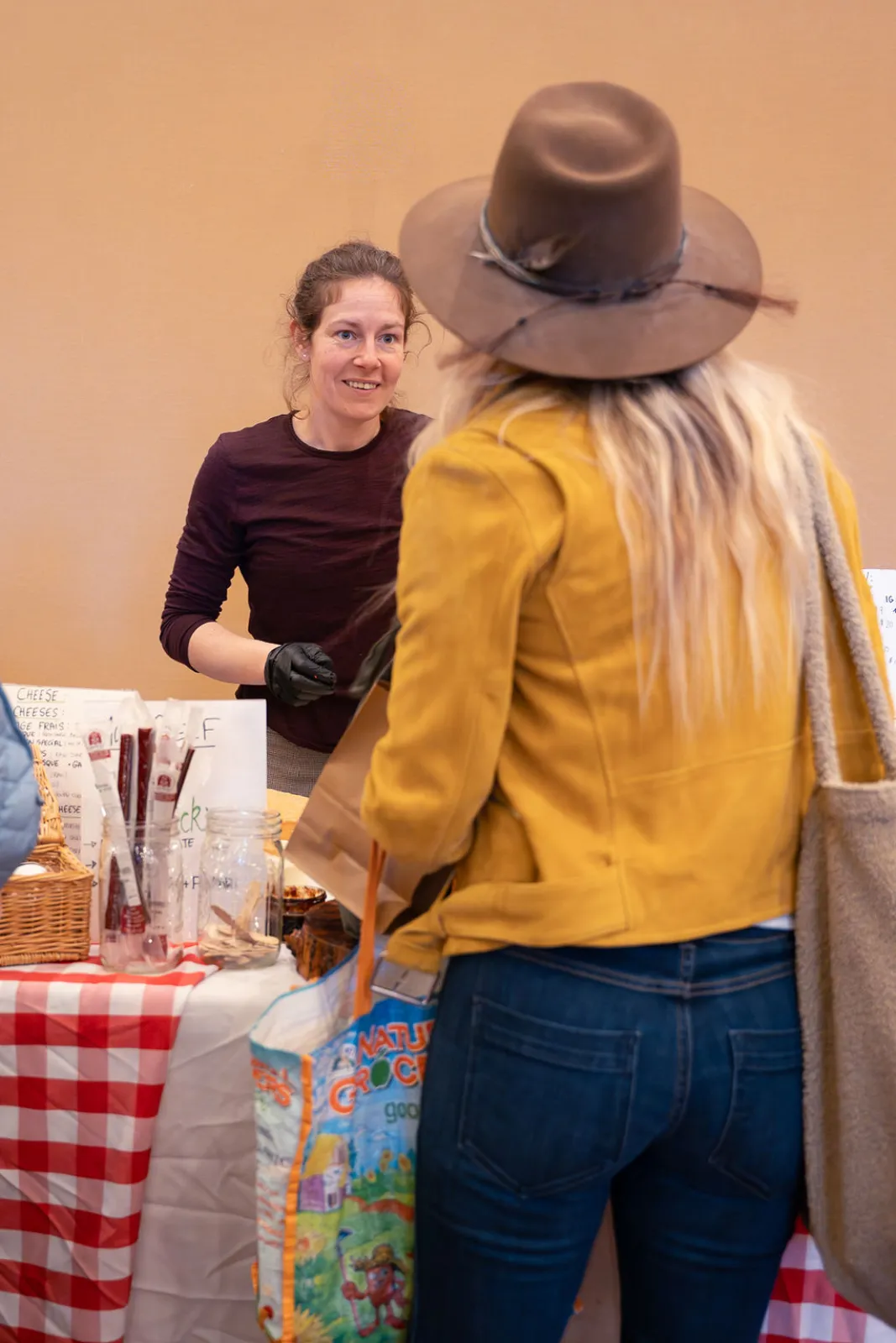 A shopper in a yellow jacket chatting with a vendor at the winter market
