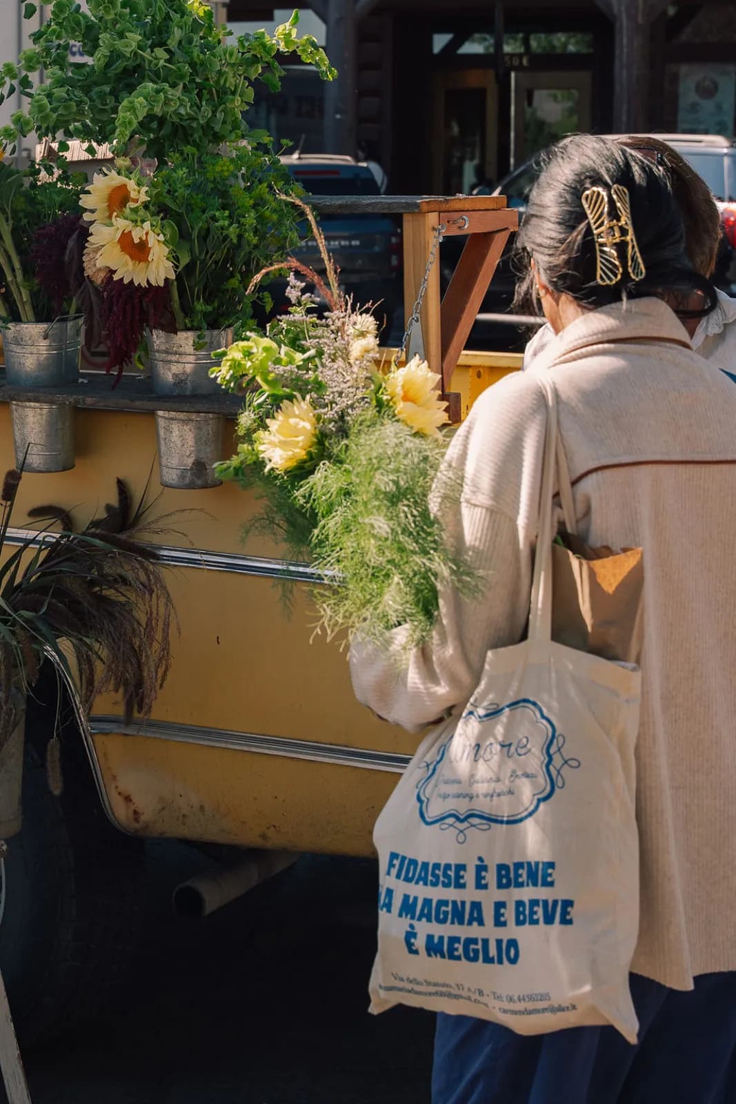 A shopper carrying a bundle of fresh flowers and a market tote